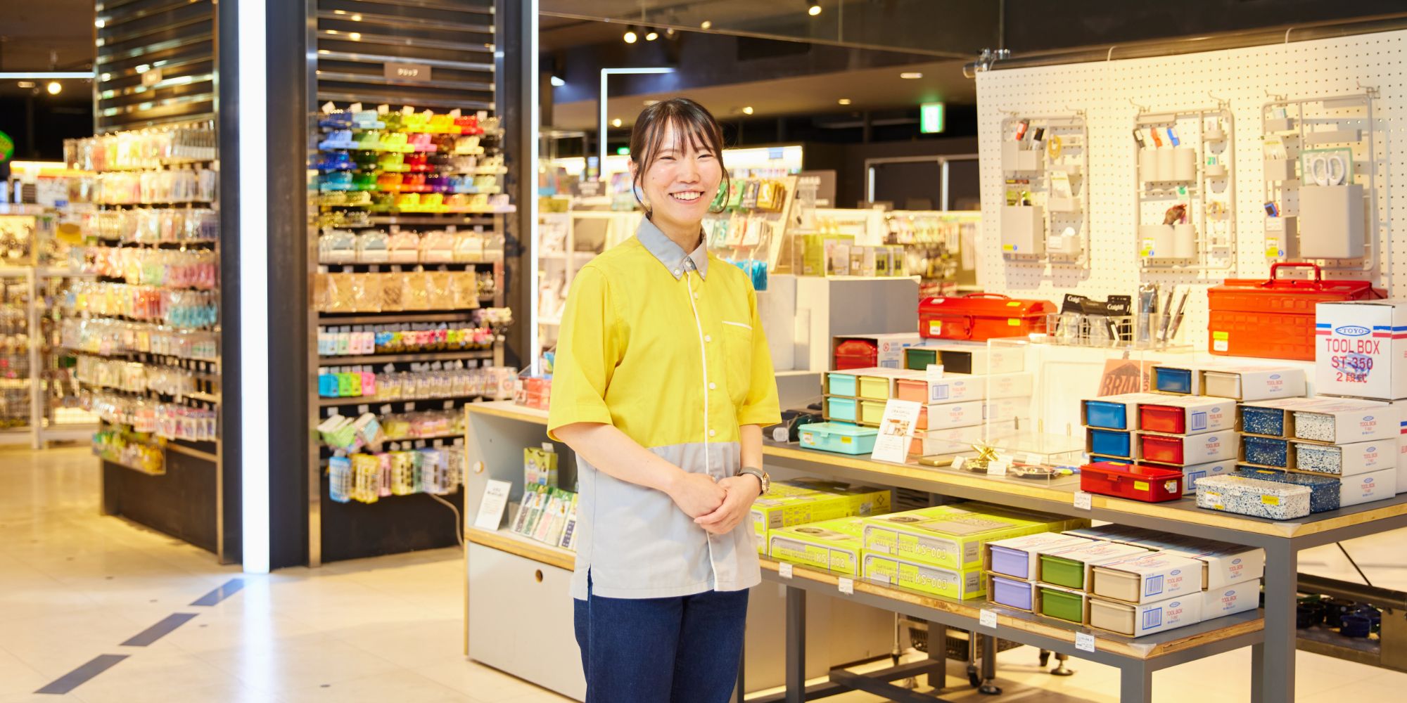 カラフルな収納箱の横で笑顔で立つT.Y.さん